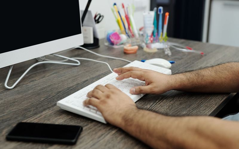 Mãos digitando uma mensagem no celular sobre uma mesa de trabalho